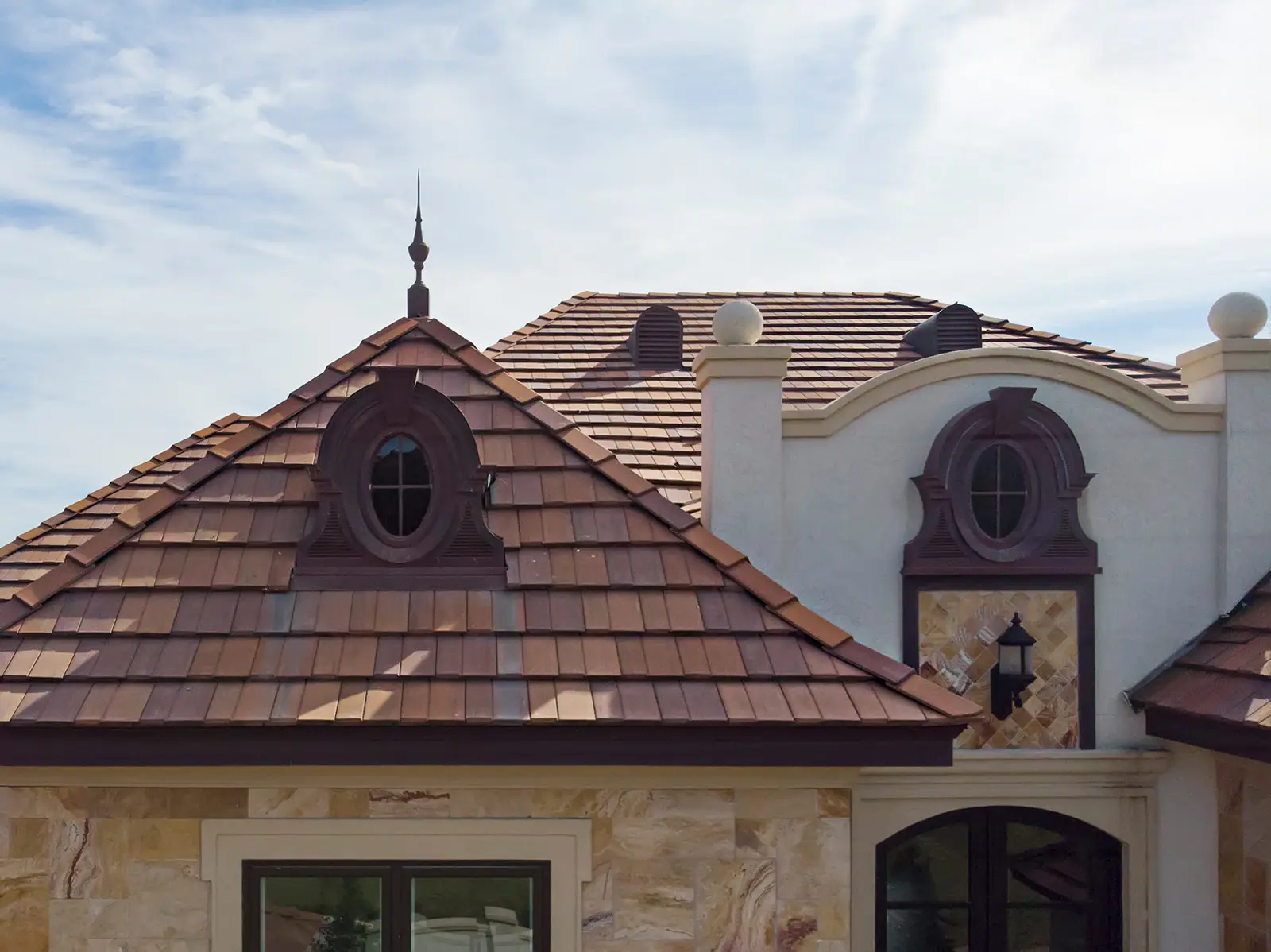 Flat concrete tile roof with oval dormer windows on a stucco home under a partly cloudy sky