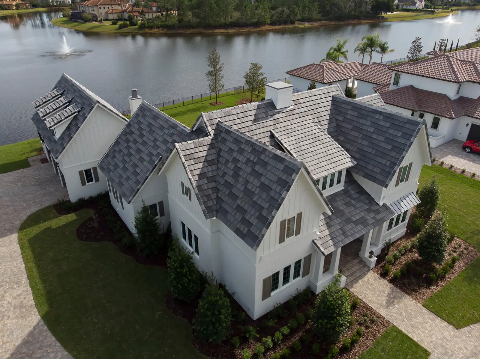 Aerial view of a newly built white lakefront home with a gray flat tile roof installed by Cache Roofing in Northeast Florida