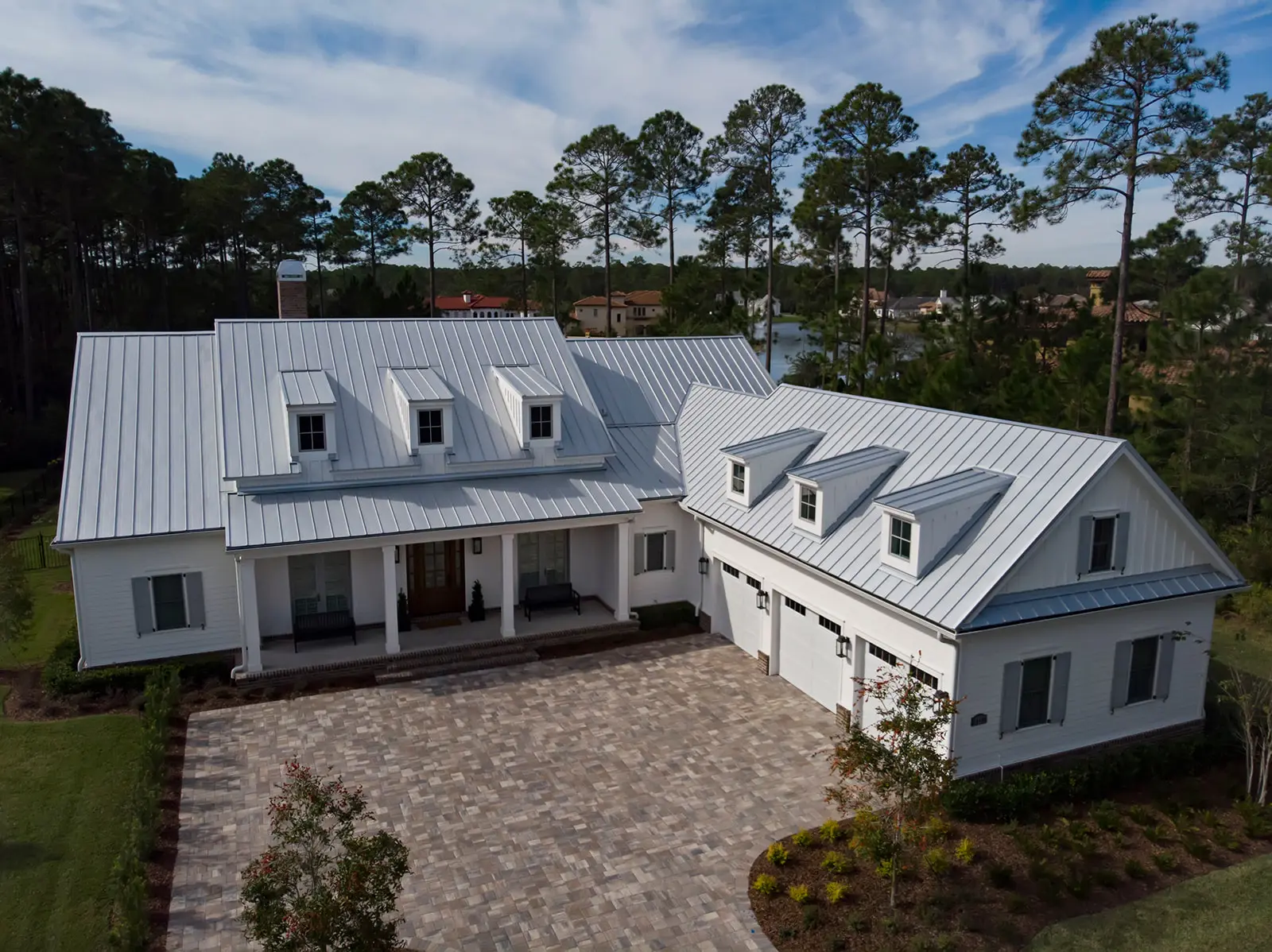 Aerial view of a white farmhouse-style home with a standing seam metal roof and dormers installed by Cache Roofing in Northeast Florida