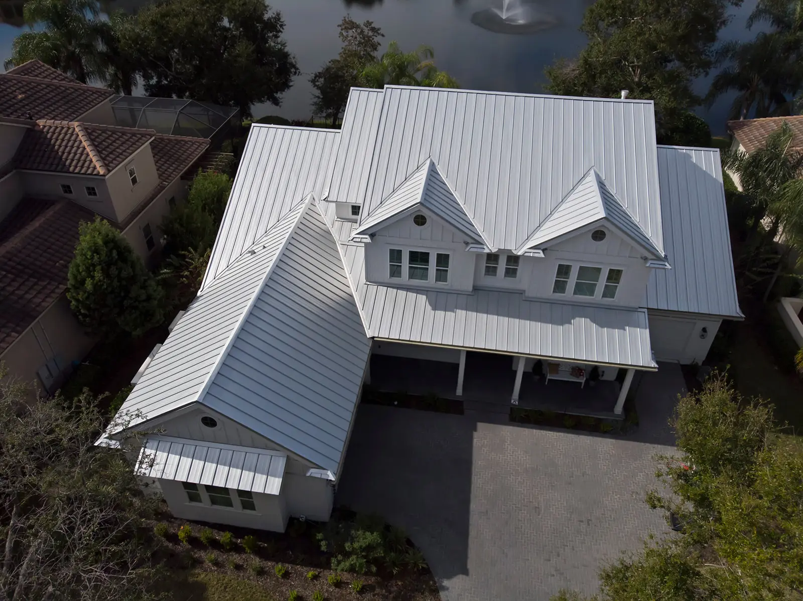 White standing seam metal roof on a two-story coastal home with dormers and a covered porch