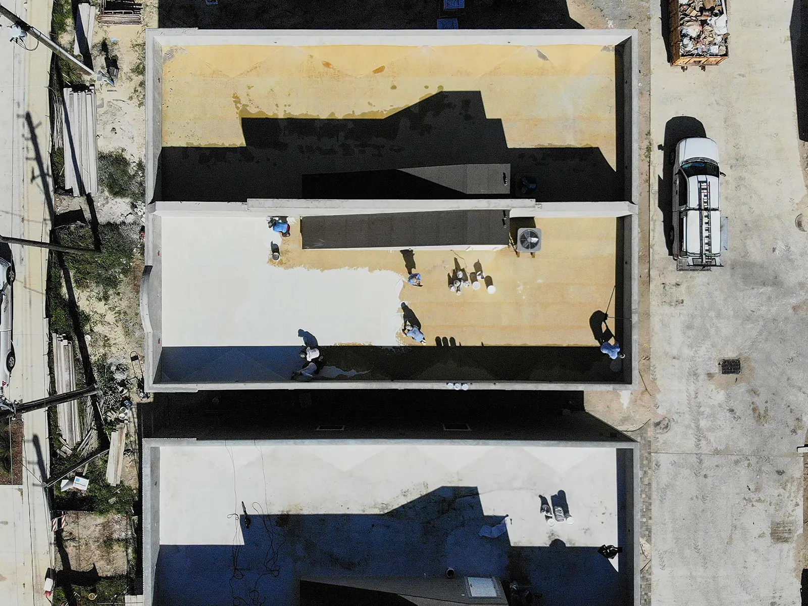 Drone view of Cache Roofing crews coating three flat commercial roofs in Jacksonville with a work truck parked alongside