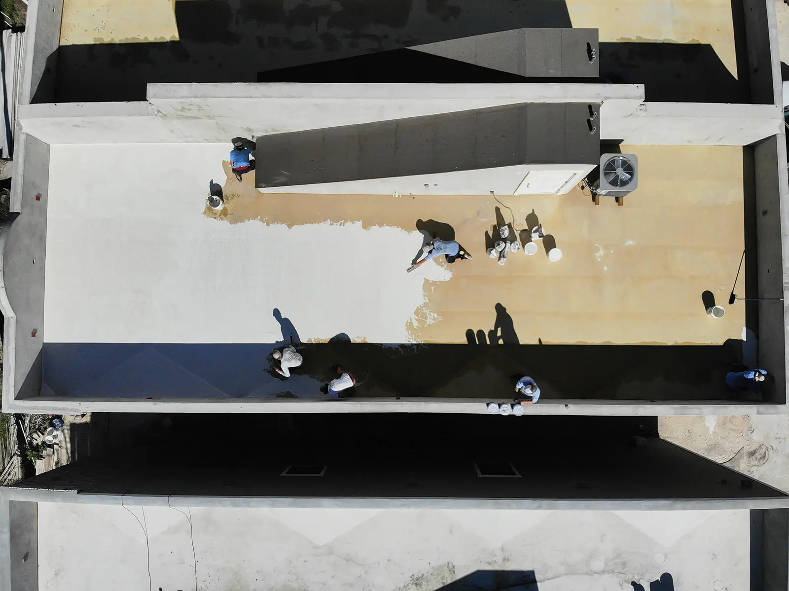 Aerial view of a Cache Roofing crew applying a white coating to a flat commercial roof in Jacksonville